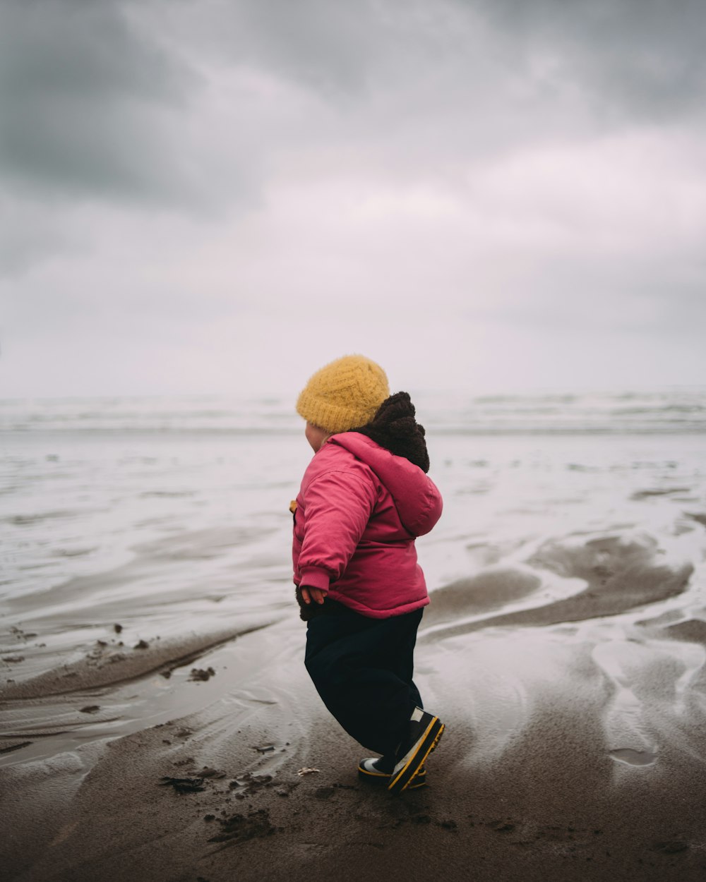 person in red hoodie and yellow knit cap walking on beach during daytime