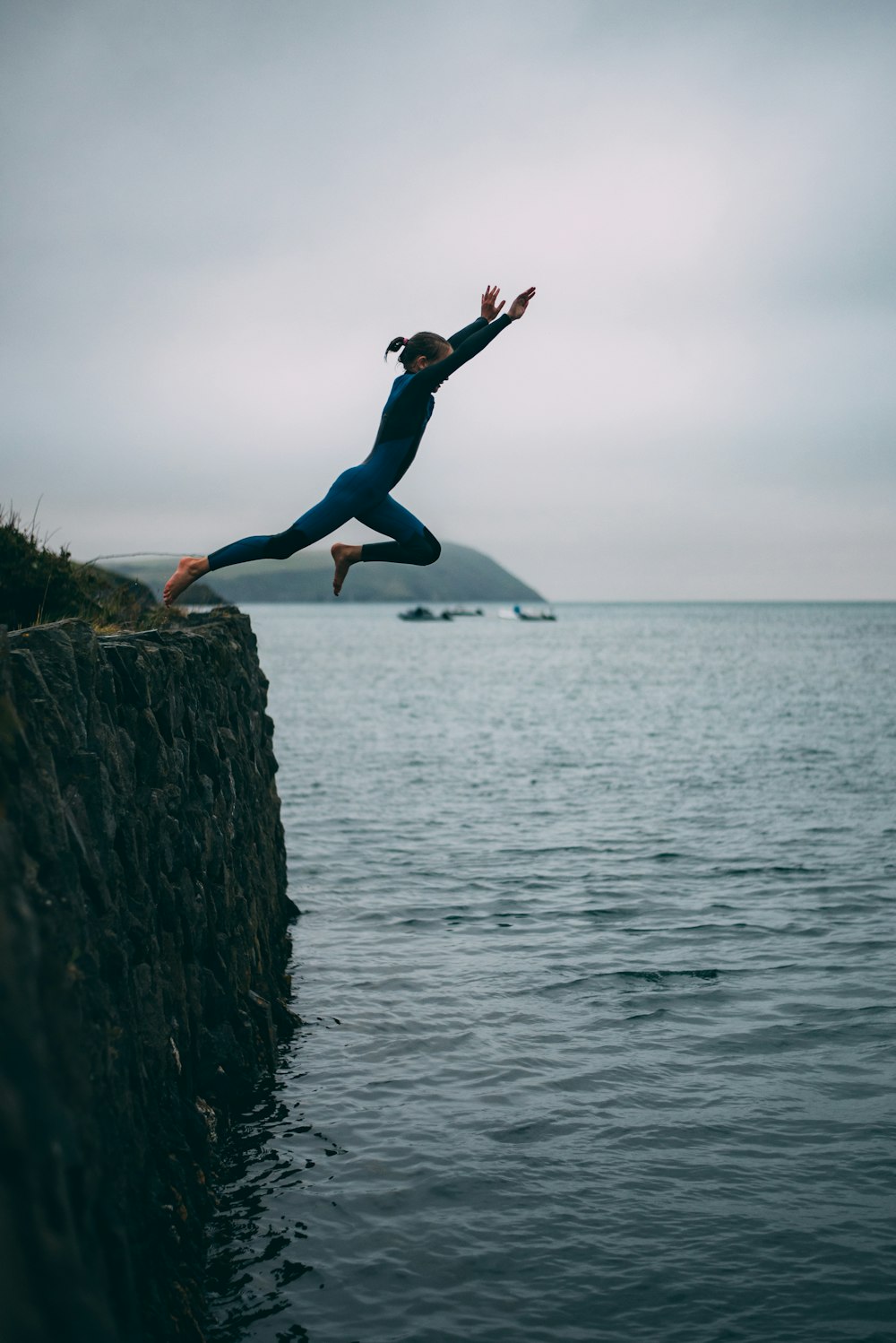 woman in blue leggings and black shirt jumping on rock near sea during daytime