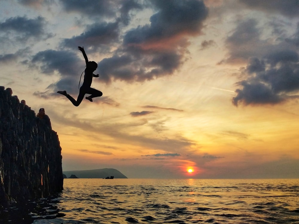 silhouette of man jumping on sea during sunset