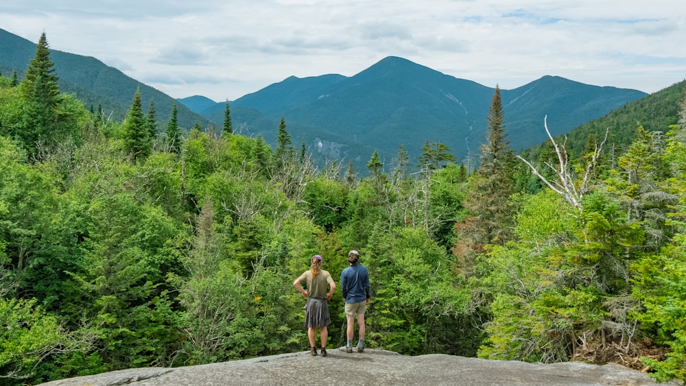 2 men walking on road near green trees and mountain during daytime