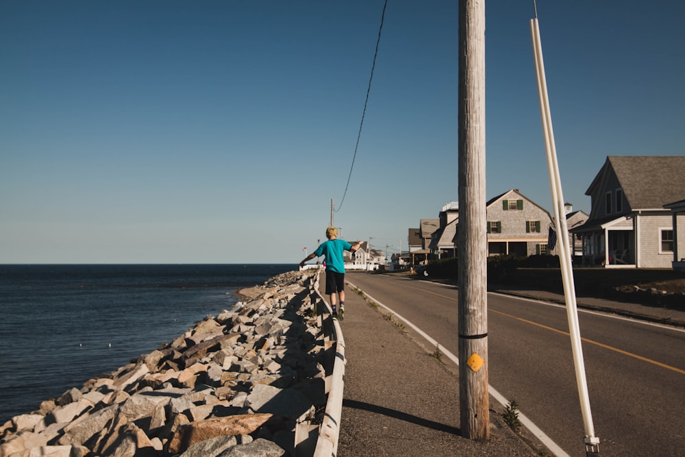 person in green shirt walking on sidewalk near body of water during daytime