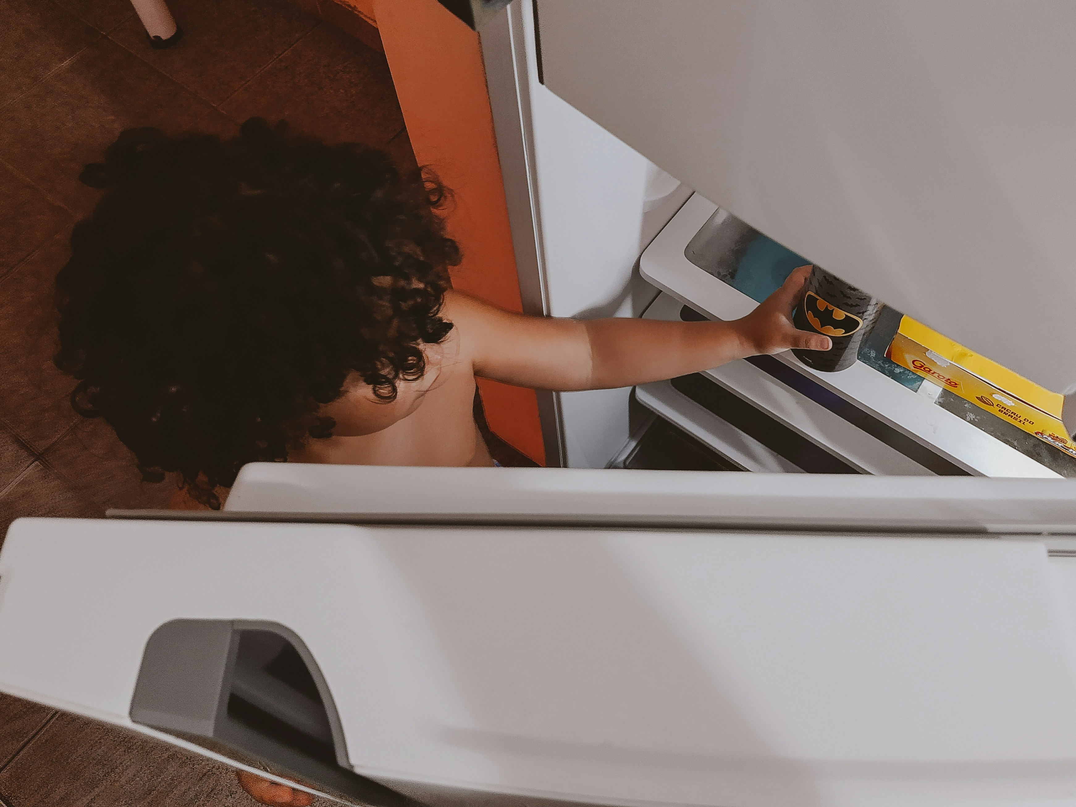 Child helping to unload a dishwasher in a bright family kitchen, star chart on the fridge
