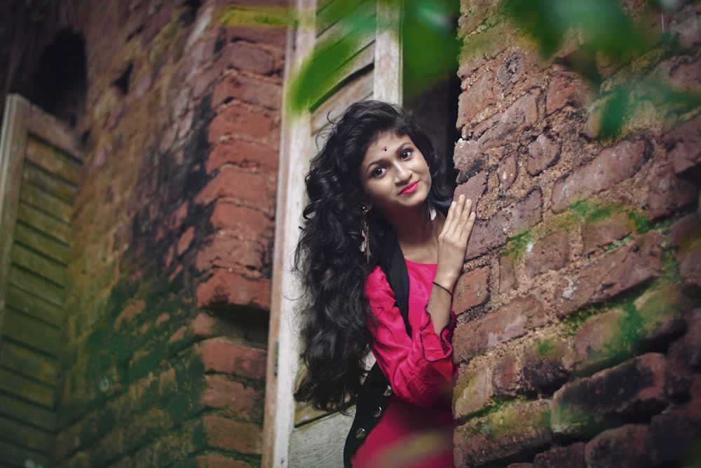 woman in pink long sleeve shirt standing beside brown brick wall