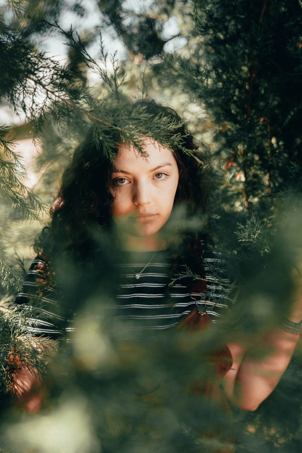 woman in black and white striped shirt standing beside green tree