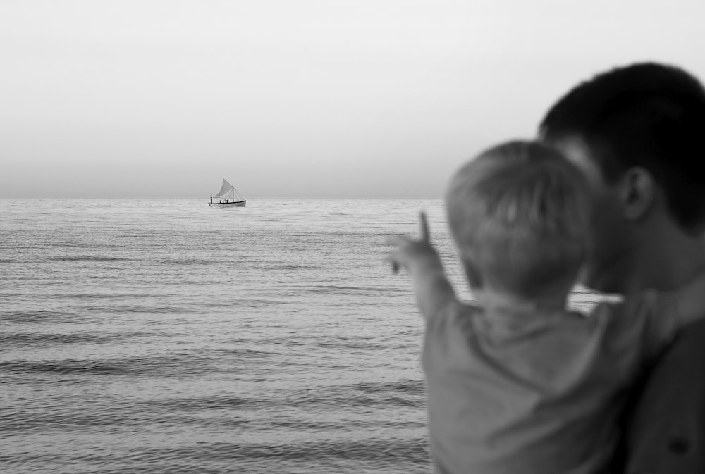 grayscale photo of boy in hoodie standing on beach