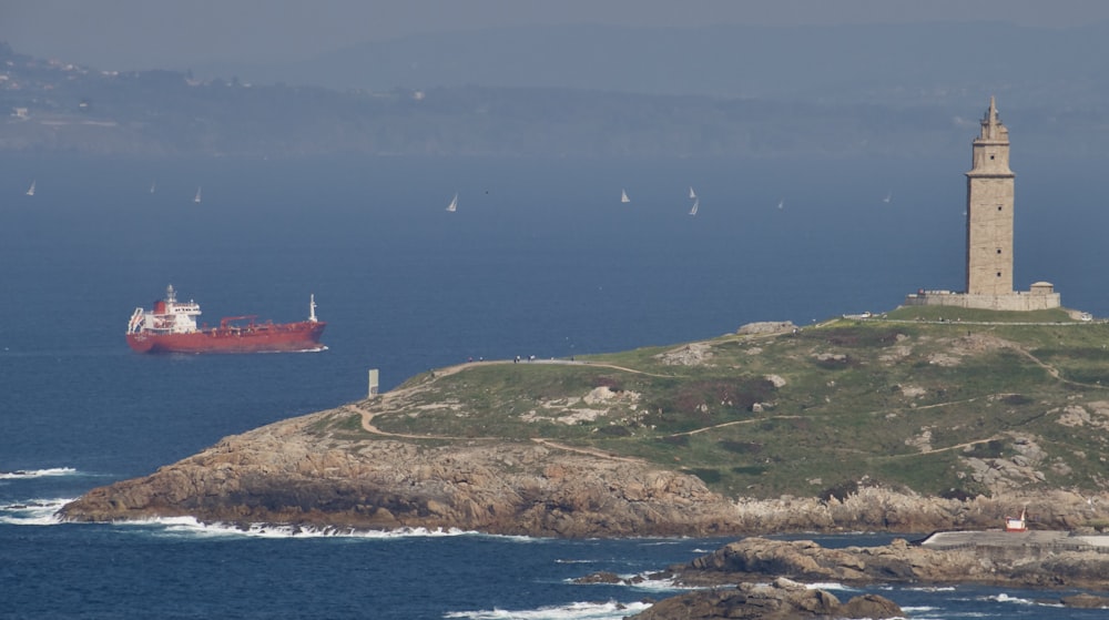 red and white lighthouse on green grass covered hill by the sea during daytime