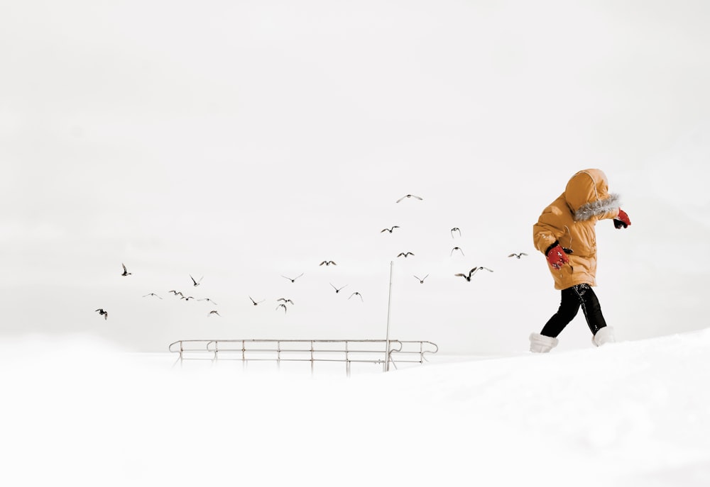 オレンジ色のジャケットと黒いズボンを着た人が昼間、雪に覆われた地面を歩いている
