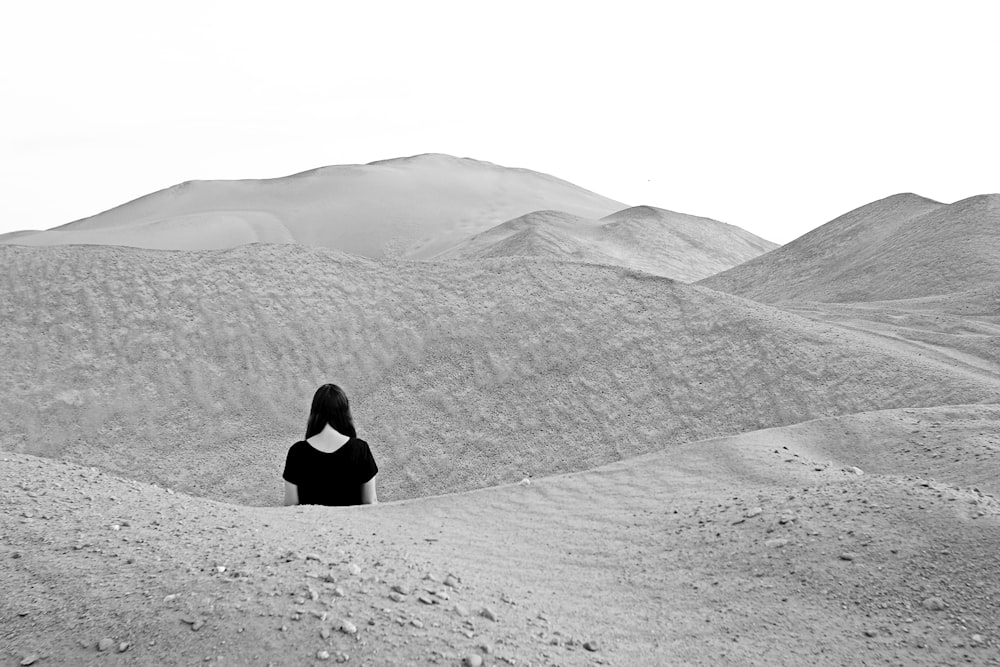 Mujer con camisa negra de manga larga sentada en arena gris durante el día