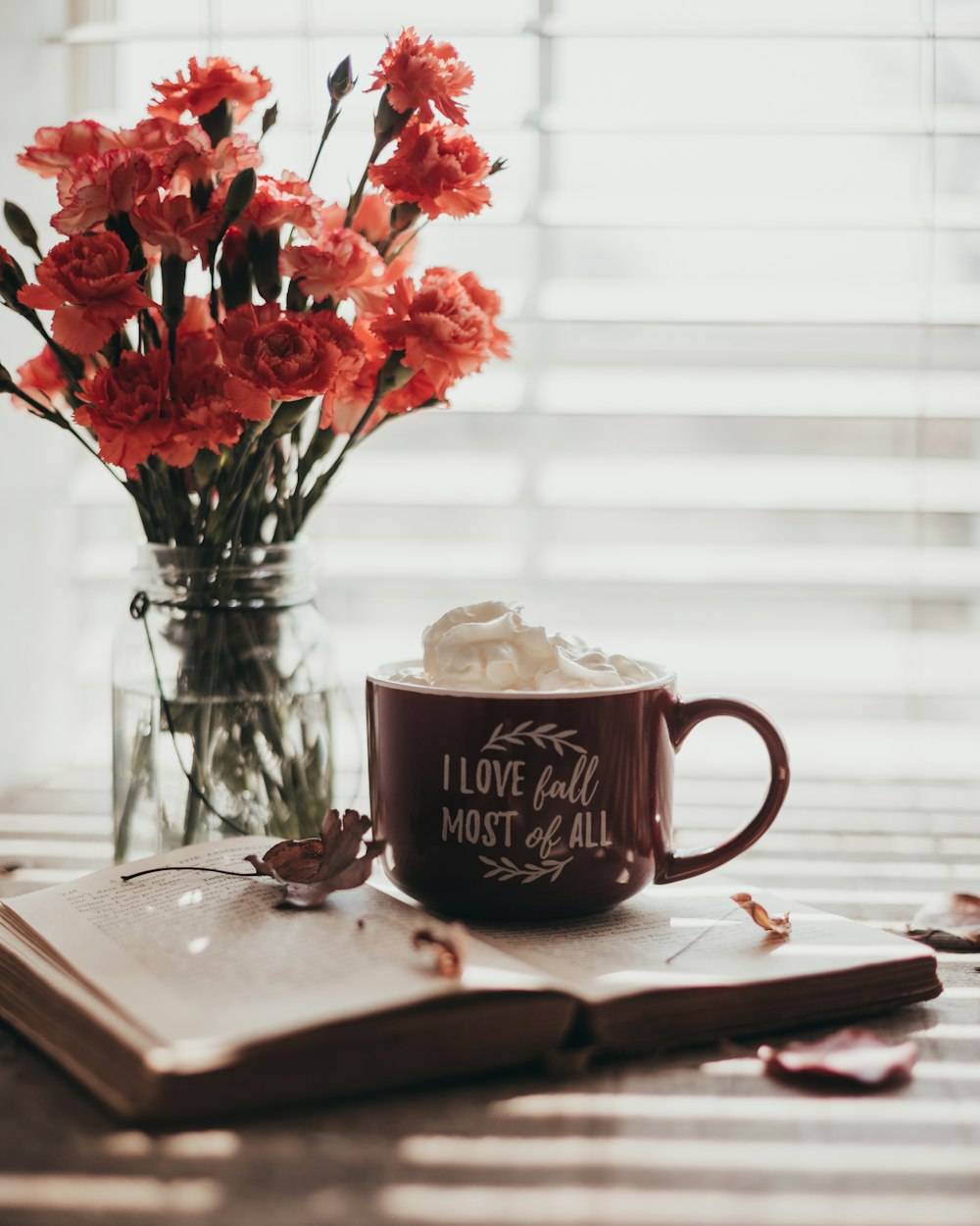 red roses in clear glass vase beside brown ceramic mug on brown wooden table