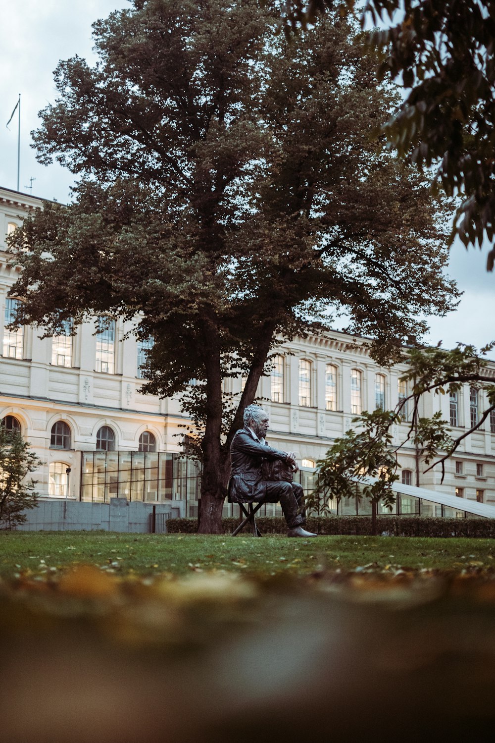 man in black jacket sitting on green grass field near white concrete building during daytime