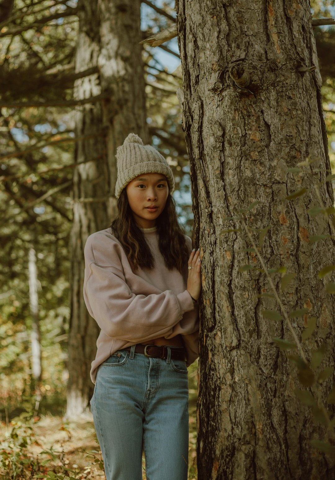 woman in gray knit cap and gray hoodie standing beside brown tree during daytime