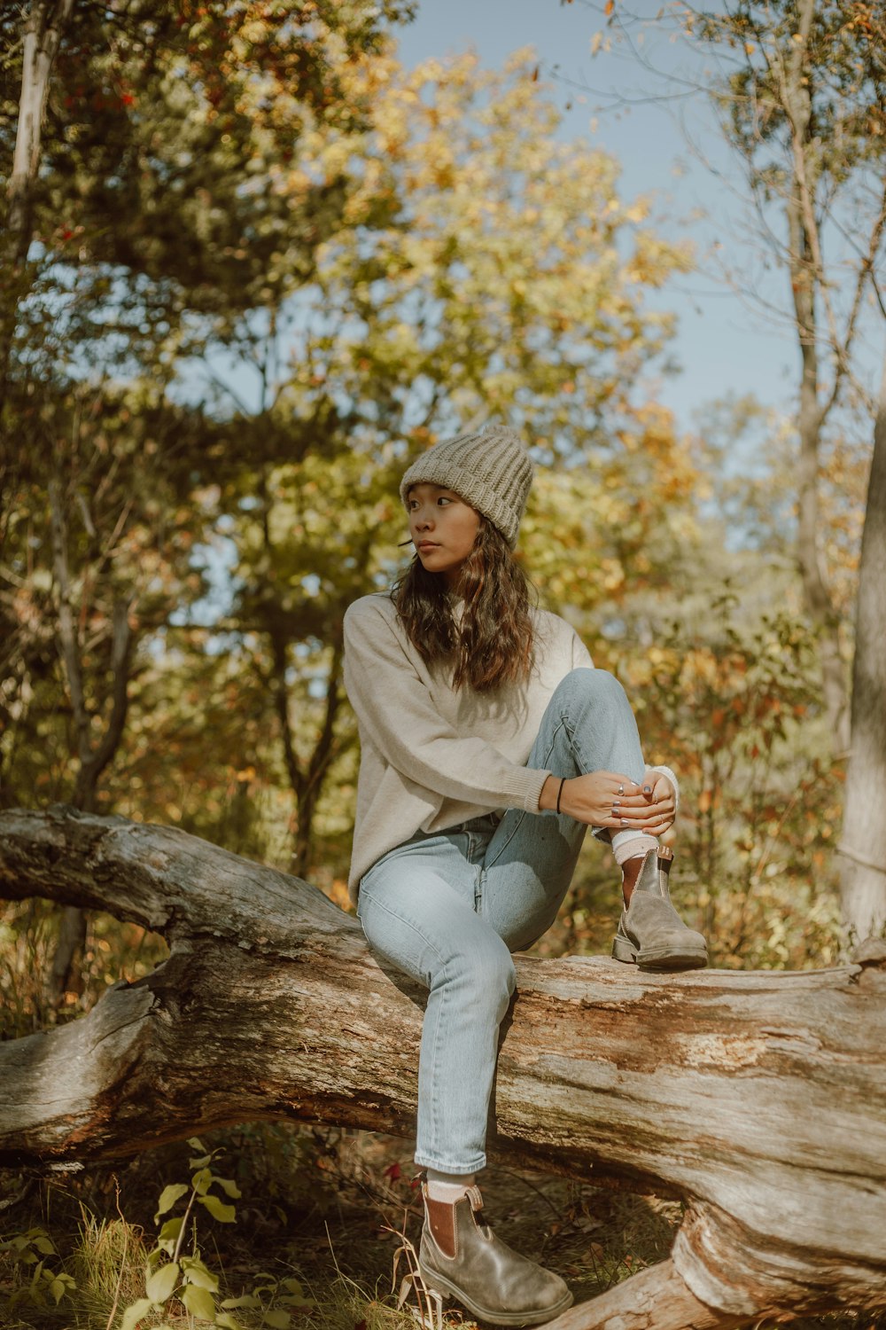 woman in white long sleeve shirt and blue denim jeans sitting on brown tree log during