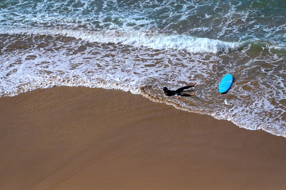Person im schwarzen Neoprenanzug, die tagsüber ein rotes Surfbrett am Strand hält
