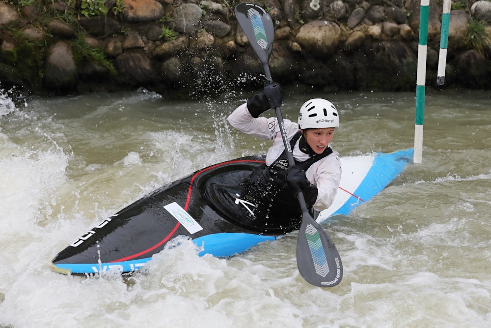 man in black and white wet suit riding on blue and red kayak