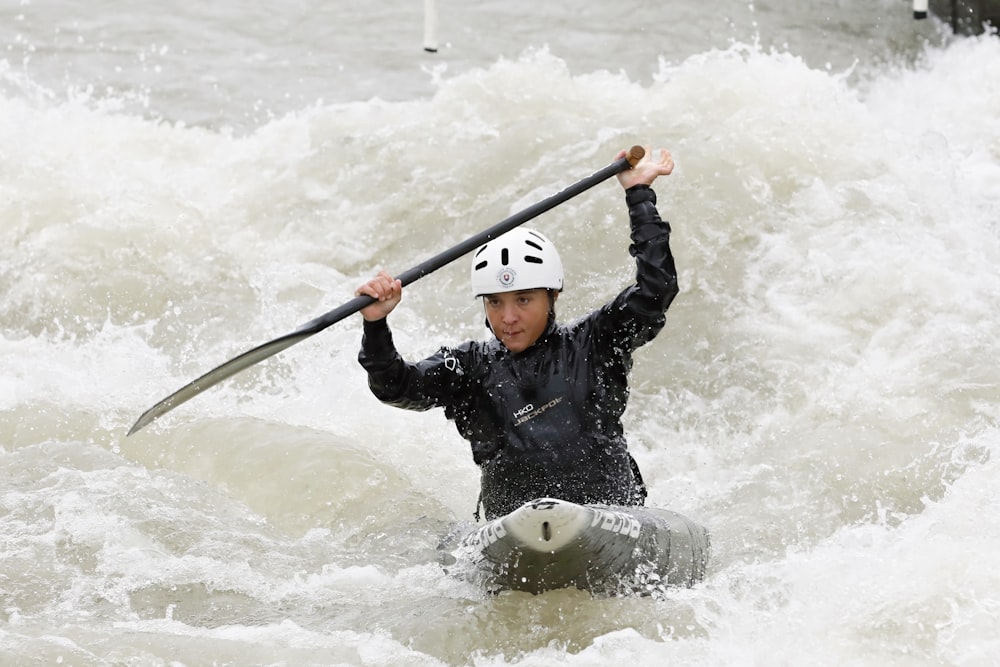 man in black jacket and white helmet riding on white and black kayak on water during