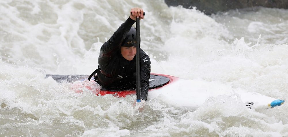 man in black jacket riding red kayak on water