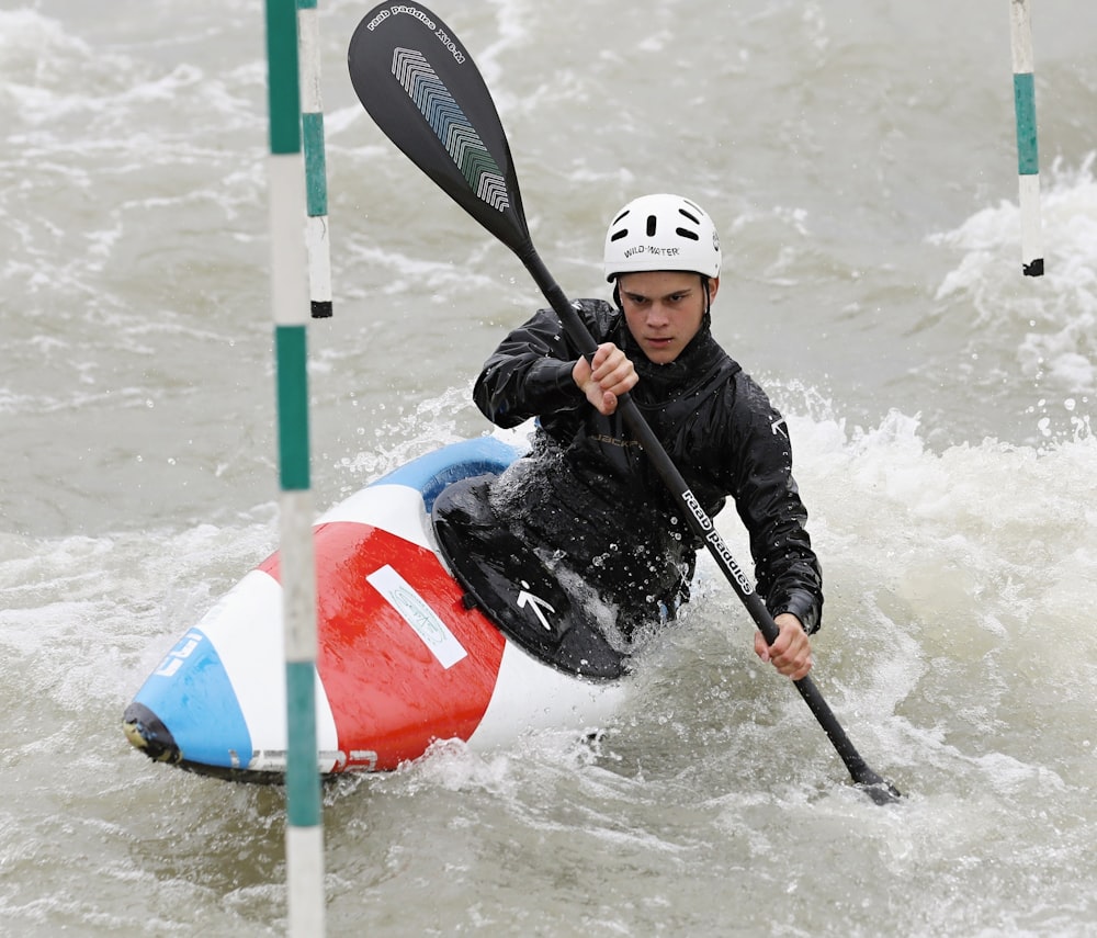 man in black jacket riding red white and blue kayak