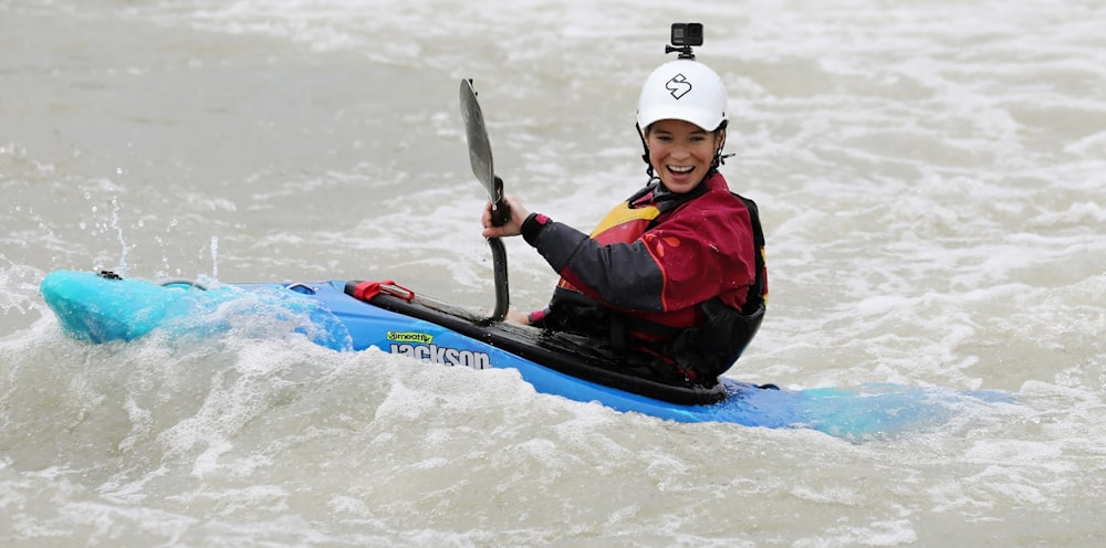 man in red and black vest riding on blue kayak