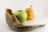 A shofar, a green apple, and a honey jar with a bee figurine on top are arranged against a plain background.