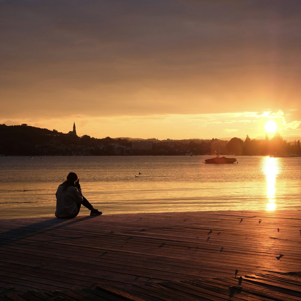 silhouette of person sitting on wooden dock during sunset