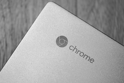 A close-up shot of a silver laptop showing the word 'chrome' and the Chrome logo on its metallic surface. The background is a blurred wooden texture, creating a contrast with the smooth and sleek surface of the device.