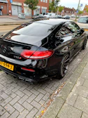 Side view of a sleek black car with tinted windows parked on a sunny street.