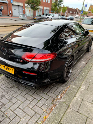 Side view of a sleek black car with tinted windows parked on a sunny street.