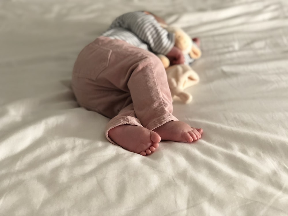 회색과 흰색 줄무늬 긴 소매 셔츠와 흰색 침대에 누워 있는 분홍색 바지를 입은 아기