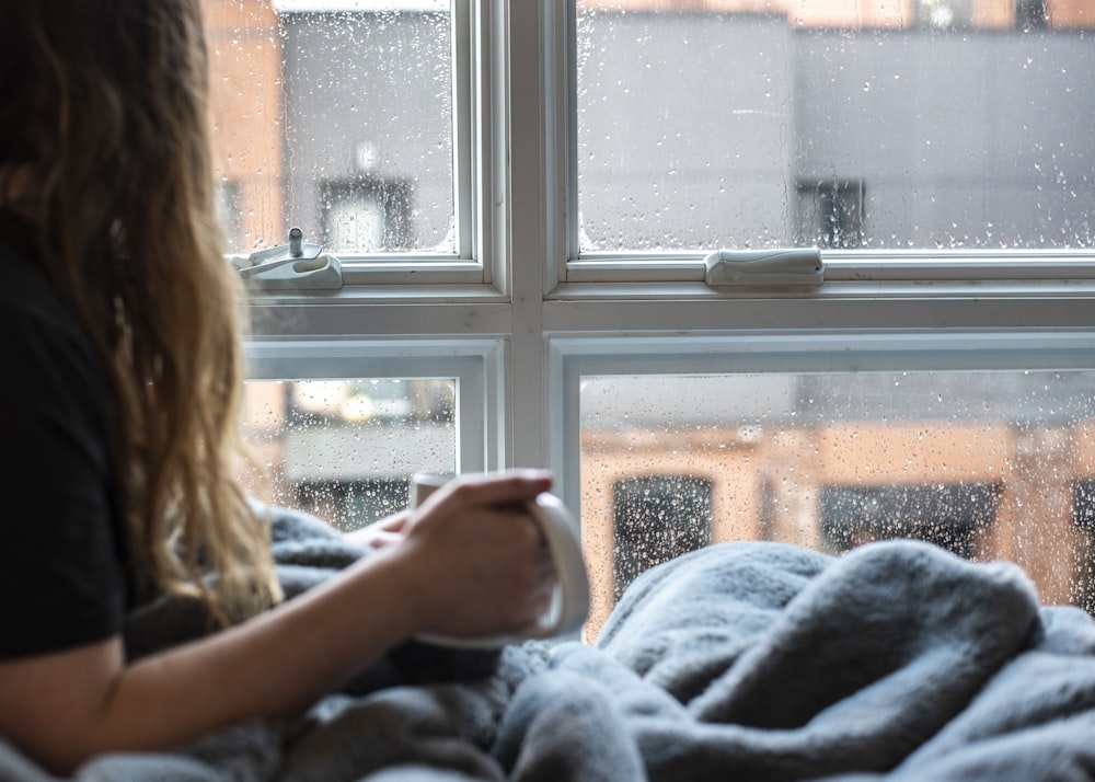 Mujer con suéter gris sentada al lado de la ventana