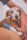 A small brown dog with large expressive eyes is held gently by a person's arm. The dog's fur is short and light brown, and it appears to be sitting on someone's lap. A pregnancy test with a blue cap showing two pink lines rests on the dog's paw. The scene suggests a playful or humorous situation.