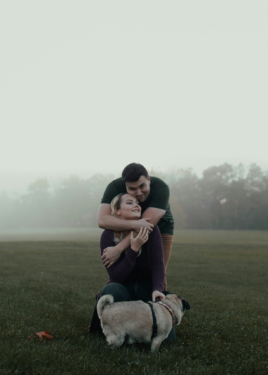 woman in maroon shirt sitting on green grass field beside white and black short coated dog