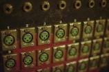 A close-up view of an old-fashioned or industrial control panel with multiple numbers, connectors, and sockets. The panel is metal, with a dark finish and some wear visible on the surface. Each connector is numbered and surrounded by a metallic frame.
