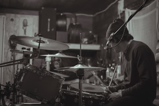 A focused musician playing drums in a cozy home studio with wooden walls.