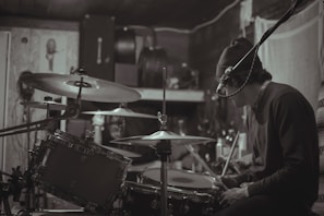 Close-up of hands playing a drum set in a dimly lit studio.