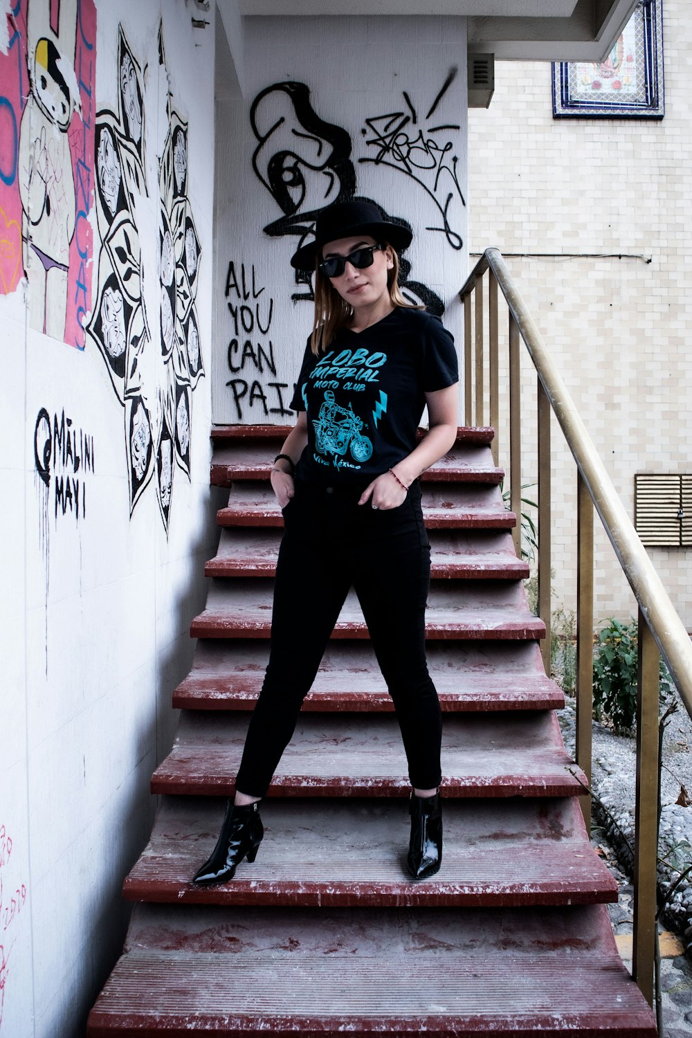 woman in green shirt and black pants wearing black hat standing on stairs