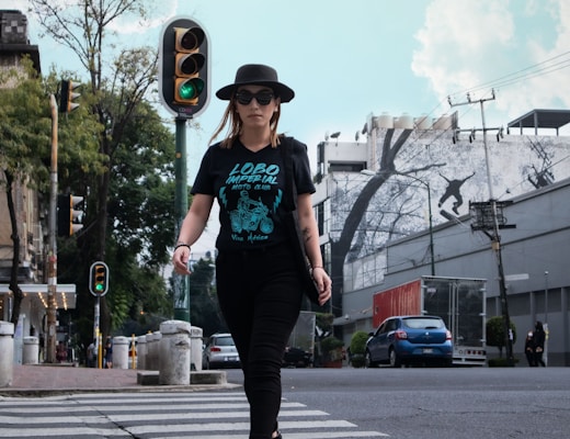 man in green t-shirt and black pants wearing black hat standing on road during daytime