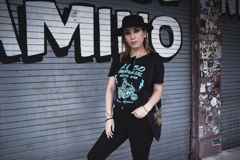 woman in black and white crew neck t-shirt and black pants standing beside black wall