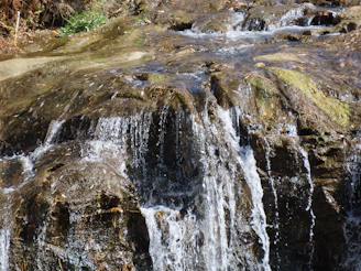 Close-up shot of water cascading over mossy rocks reflecting the summer sun at the waterfall site.