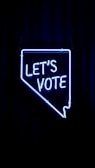 A neon sign in the shape of a state outline with the words 'LET'S VOTE' illuminated in bright blue against a dark background.