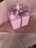 A gift box wrapped in pink paper with small black polka dots, adorned with a curly purple ribbon and a Happy Birthday tag. The box sits on top of pink tissue paper.