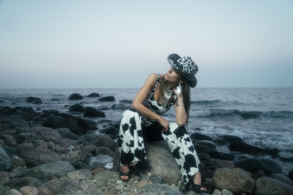 Mujer en vestido de lunares blanco y negro sentada en la roca junto al mar durante el día