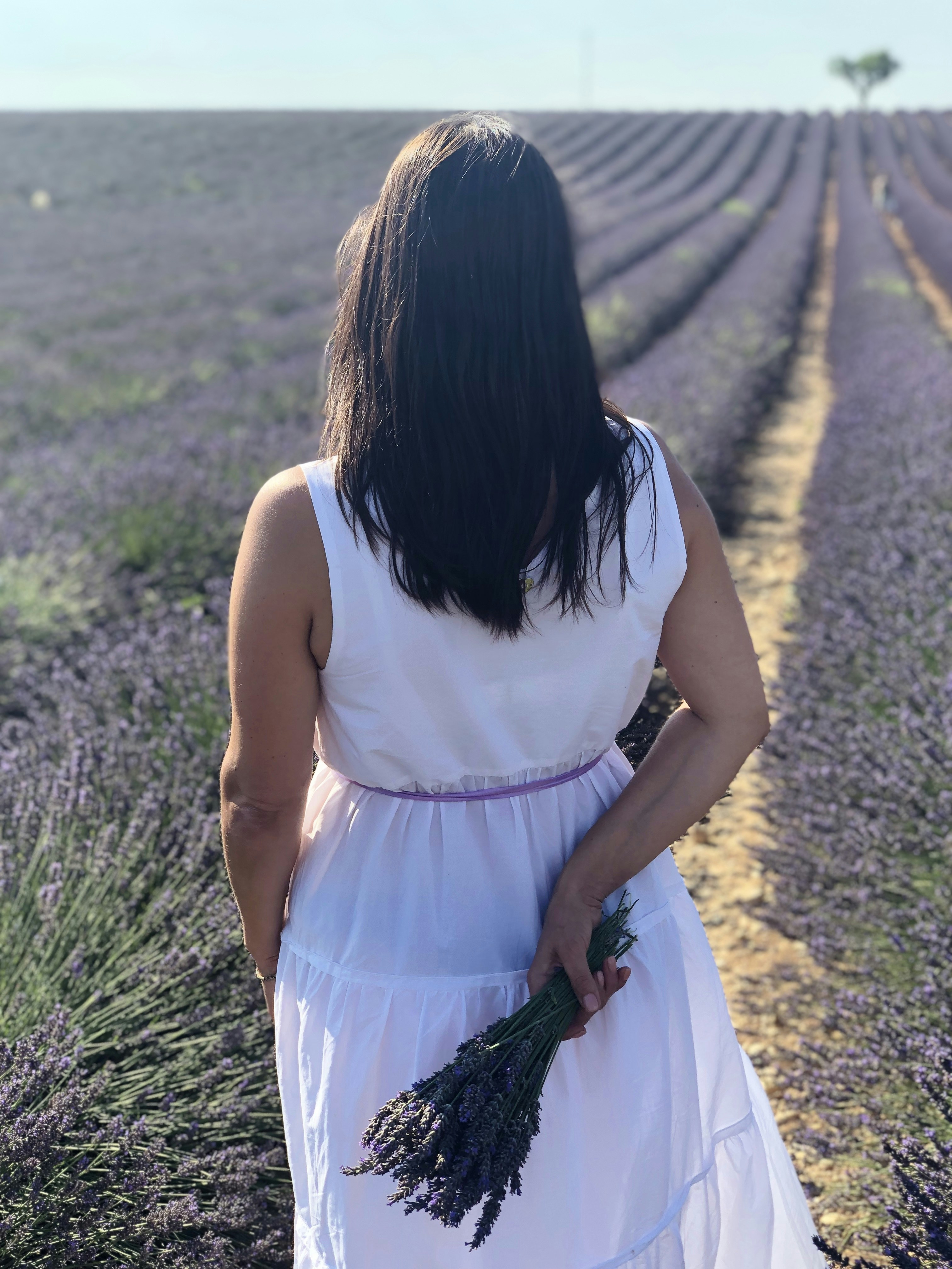 femme en robe blanche sans manches marchant sur le champ d’herbe verte pendant la journée