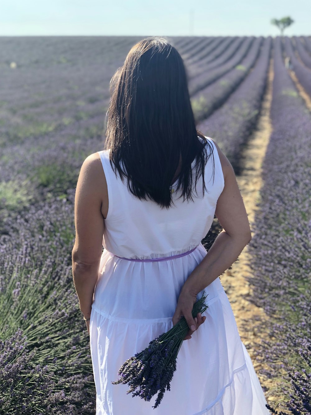 Mujer en vestido blanco sin mangas caminando en el campo de hierba verde durante el día