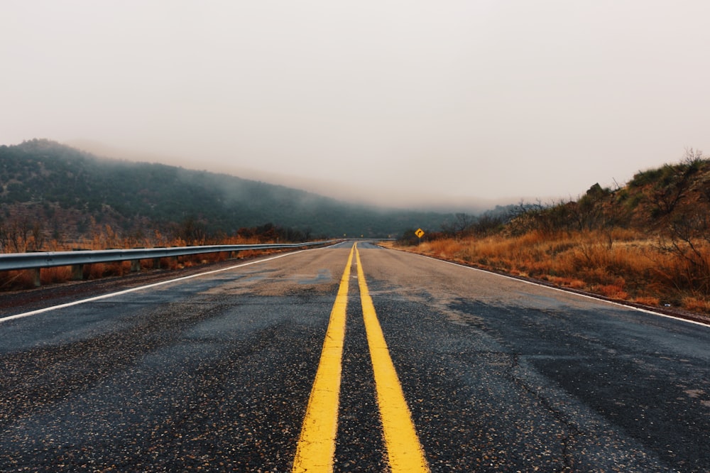 black asphalt road between brown grass field during daytime