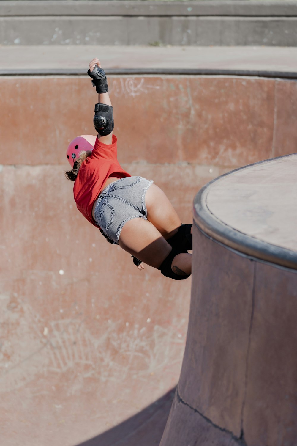 woman in red shirt and blue denim shorts doing skateboard stunts