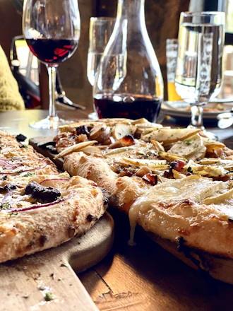 Close-up of three artisanal pizzas with fresh toppings on a rustic wooden table.