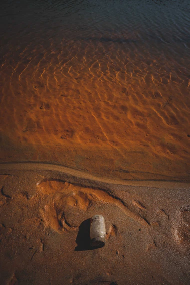 Close-up of a premium glass jar filled with authentic Ibiza sand, resting on soft beige fabric with sunlight filtering through.