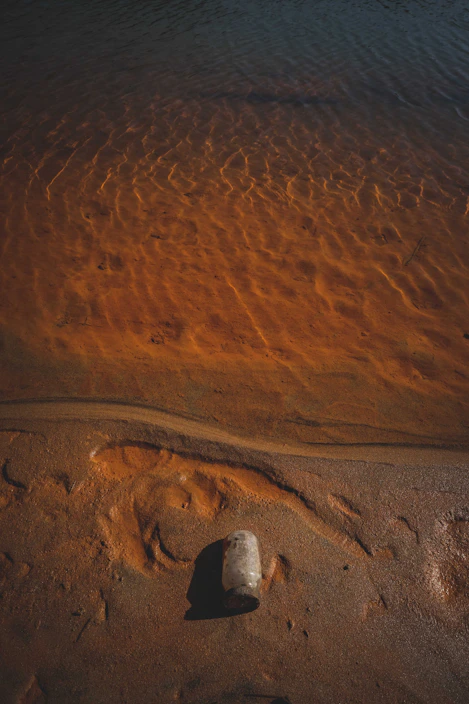 A crystal-clear bottle of Zamzam water glowing softly against a backdrop of golden desert sands at sunset.