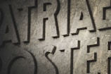 Large, carved stone letters are prominently displayed with a textured surface. The lighting casts shadows, creating depth and enhancing the rugged appearance of the stone.