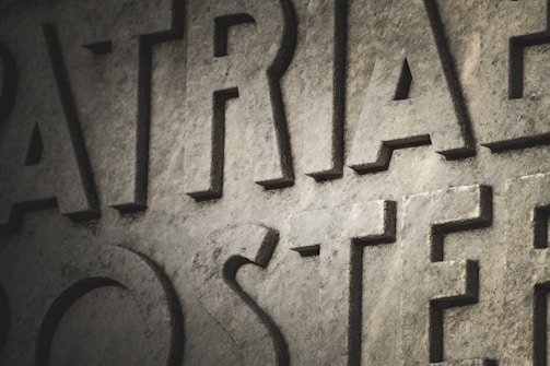 Large, carved stone letters are prominently displayed with a textured surface. The lighting casts shadows, creating depth and enhancing the rugged appearance of the stone.